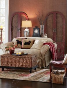 Loveseat in a beige brocade slipcover, a seagrass storage coffee table, two red scroll wall gates, and Scotty dog pillows.