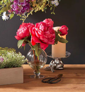 Dark pink peonies in a footed glass vase next to a lit ivory candle