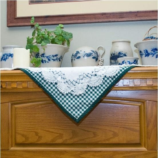A collection of gray and blue floral stoneware on a mantle with a white doily over a green check cloth.
