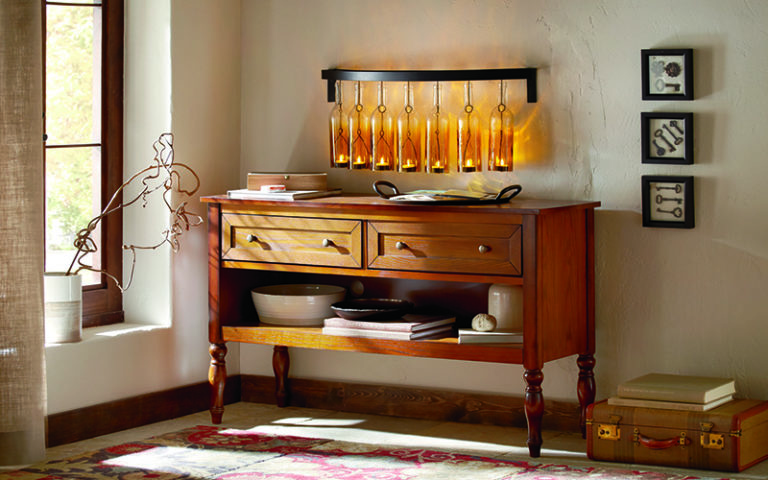 Rack of seven hanging amber colored glass bottles holding lit votives, above a wood console, by three skeleton key frames.