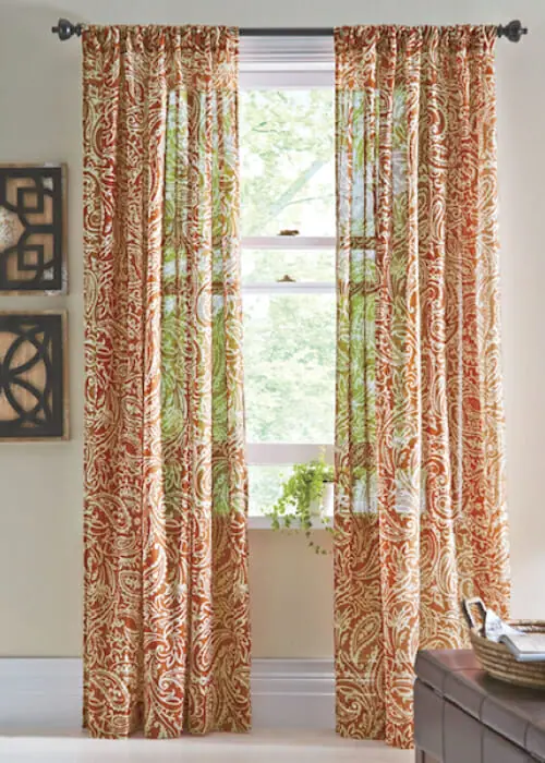 Sheer shirr-on drapes in an orange paisley pattern, by two black and wood geometric wall plaques.