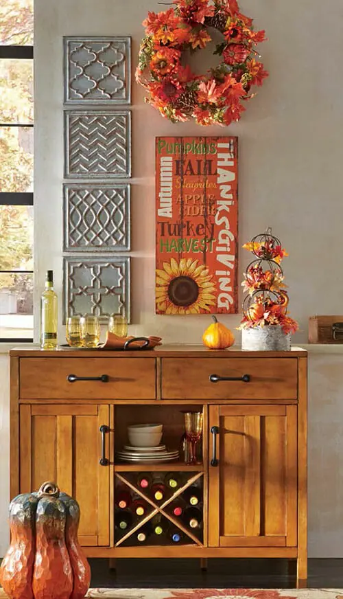 A low cabinet with a bottom wine rack, an orange floral wreath, a harvest plaque, and four embossed wall plaques.