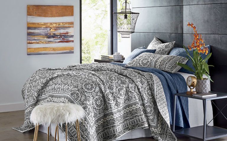 Layered navy and boho gray and white quilt sets, an orange orchid on a side table, and a gray and orange wall canvas.