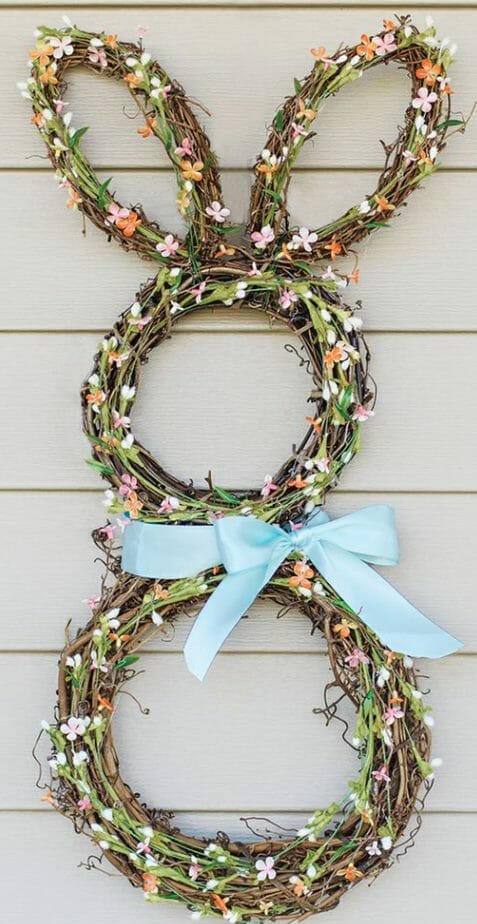 Four grapevine wreaths wrapped with pastel flower sprigs and tied with a blue ribbon to create an Easter bunny wreath.