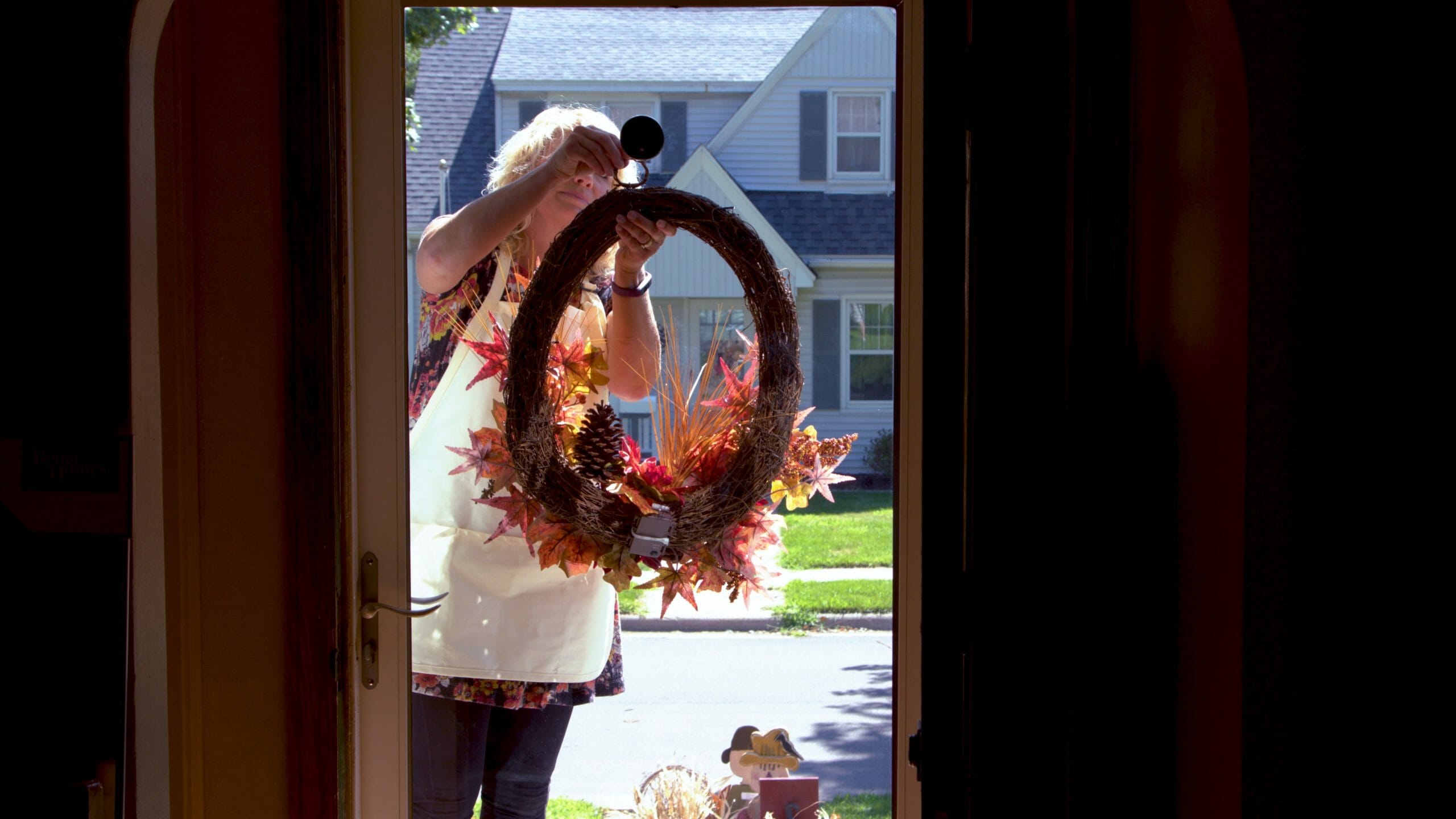 woman hanging a large wreath full of pumpkins maple leaves berries and pinecones