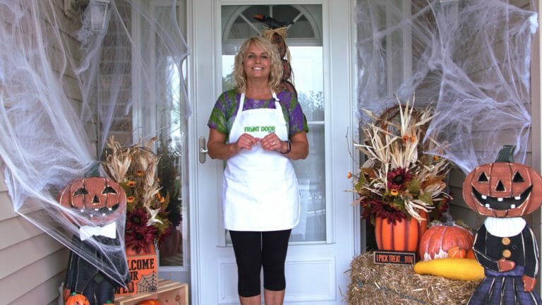 woman standing on porch with cobwebs pumpkins gourds and distressed wooden jack o lanterns and other Halloween decor