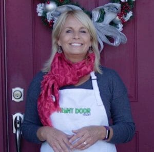 woman with red scarf standing in front of maroon door adorned with Christmas wreath