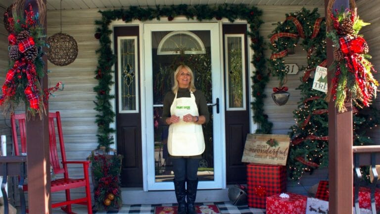 woman on porch, red rocking chair, evergreen candy cane with red plaid ribbon, garland and other Christmas décor