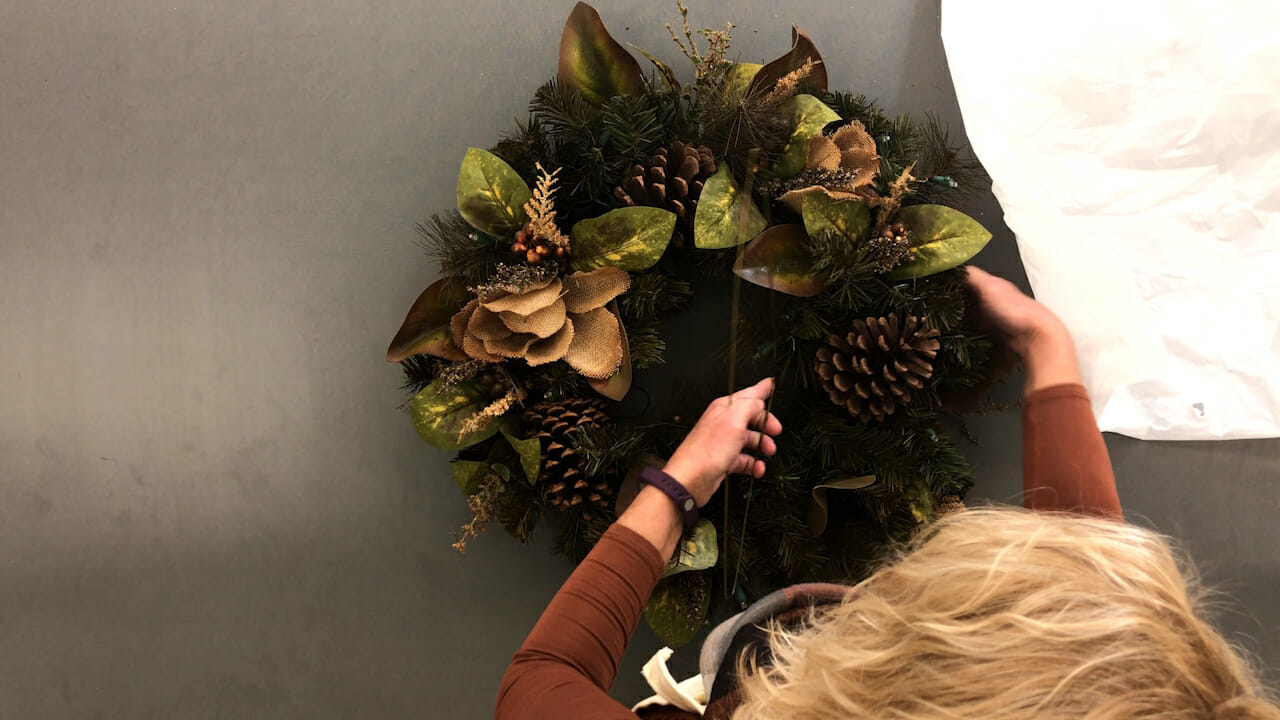 woman putting wreath on metal clothes hanger for storage