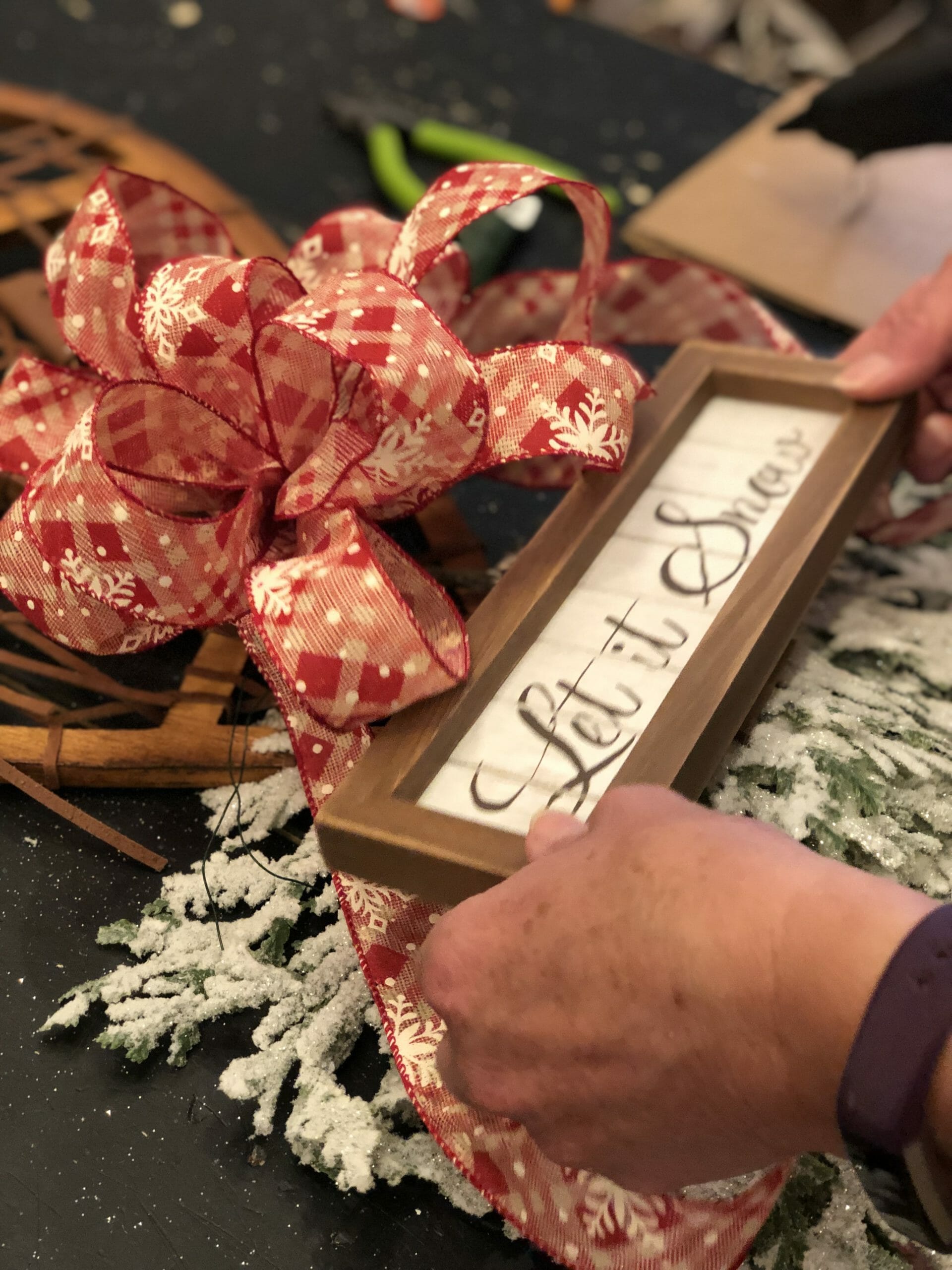woman applying let it snow sign to snow shoe wreath
