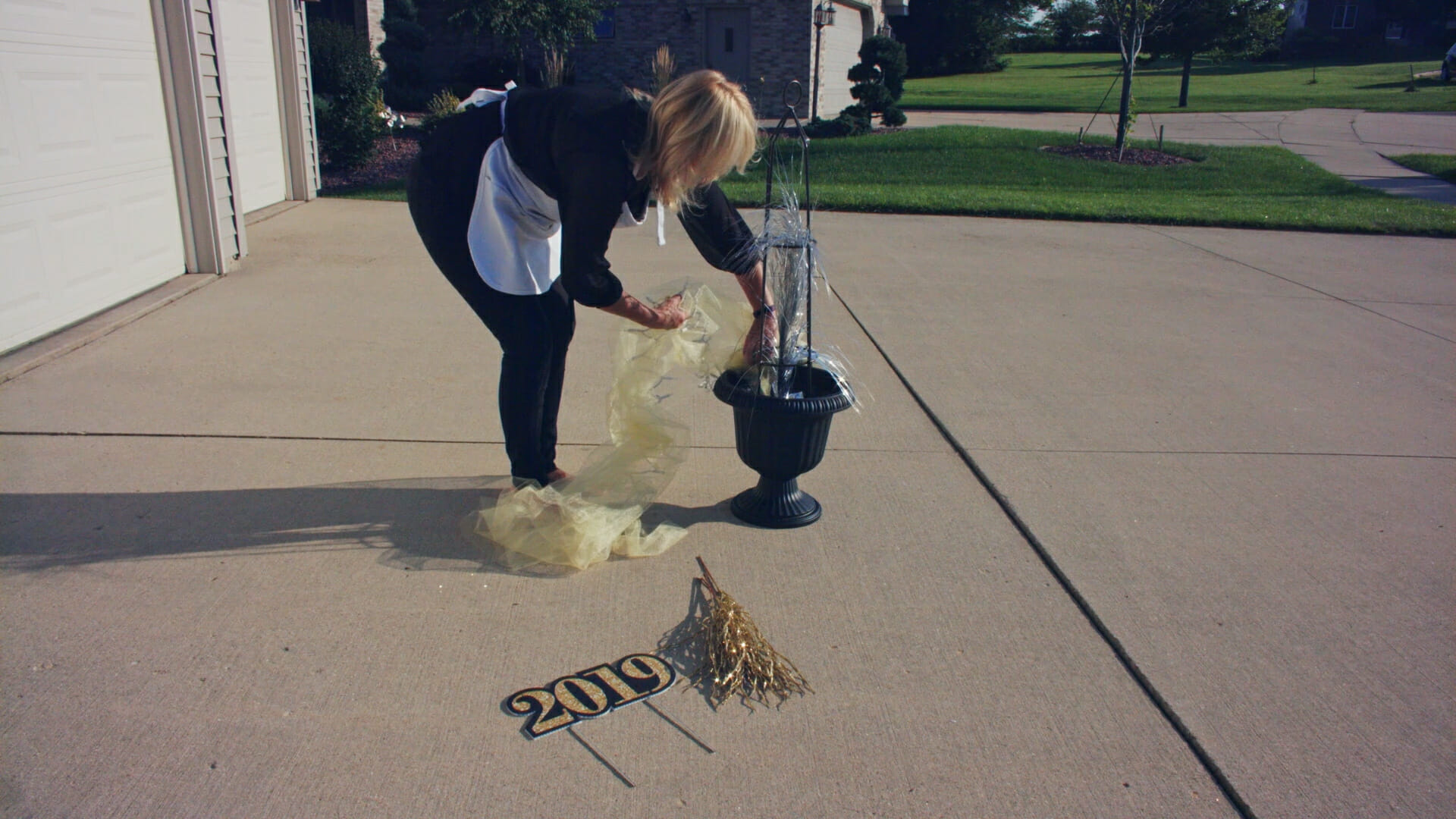 A woman putting yellow tulle and lights in a black urn planter with silver and gold 2019 New Year's Eve decor.