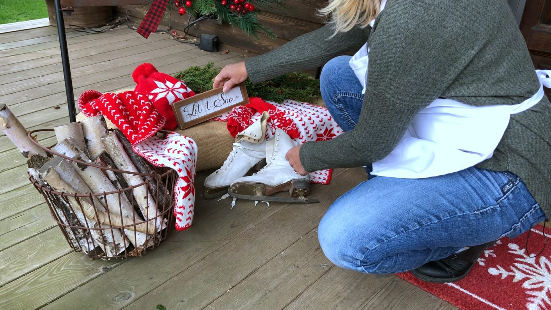 woman placing let it snow sign next to ice skates and red and white hat and scarf to create a winter holiday porch