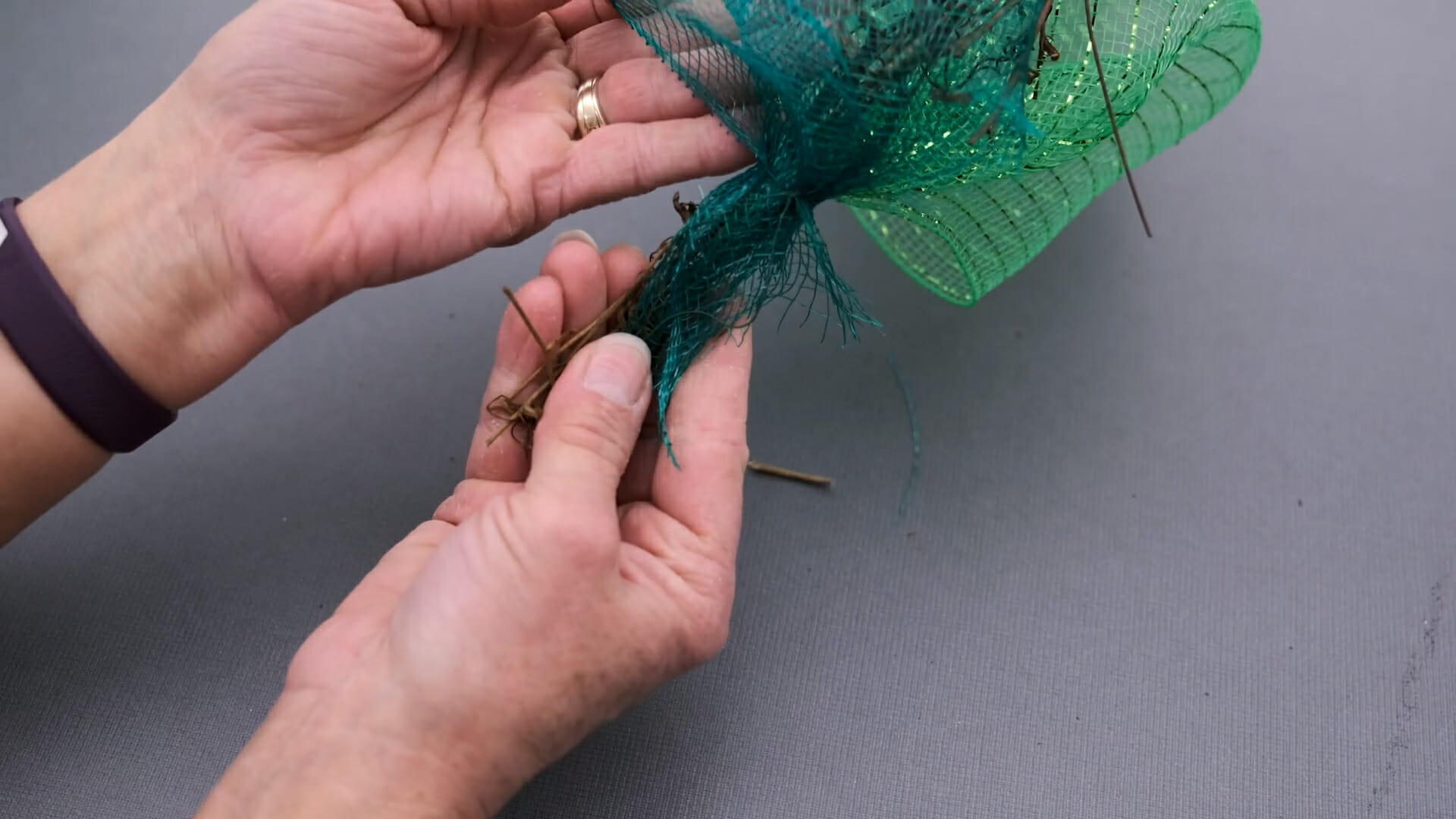 Close-up view of hands tying off the ends of two shades of green netting on a narrow grapevine garland.