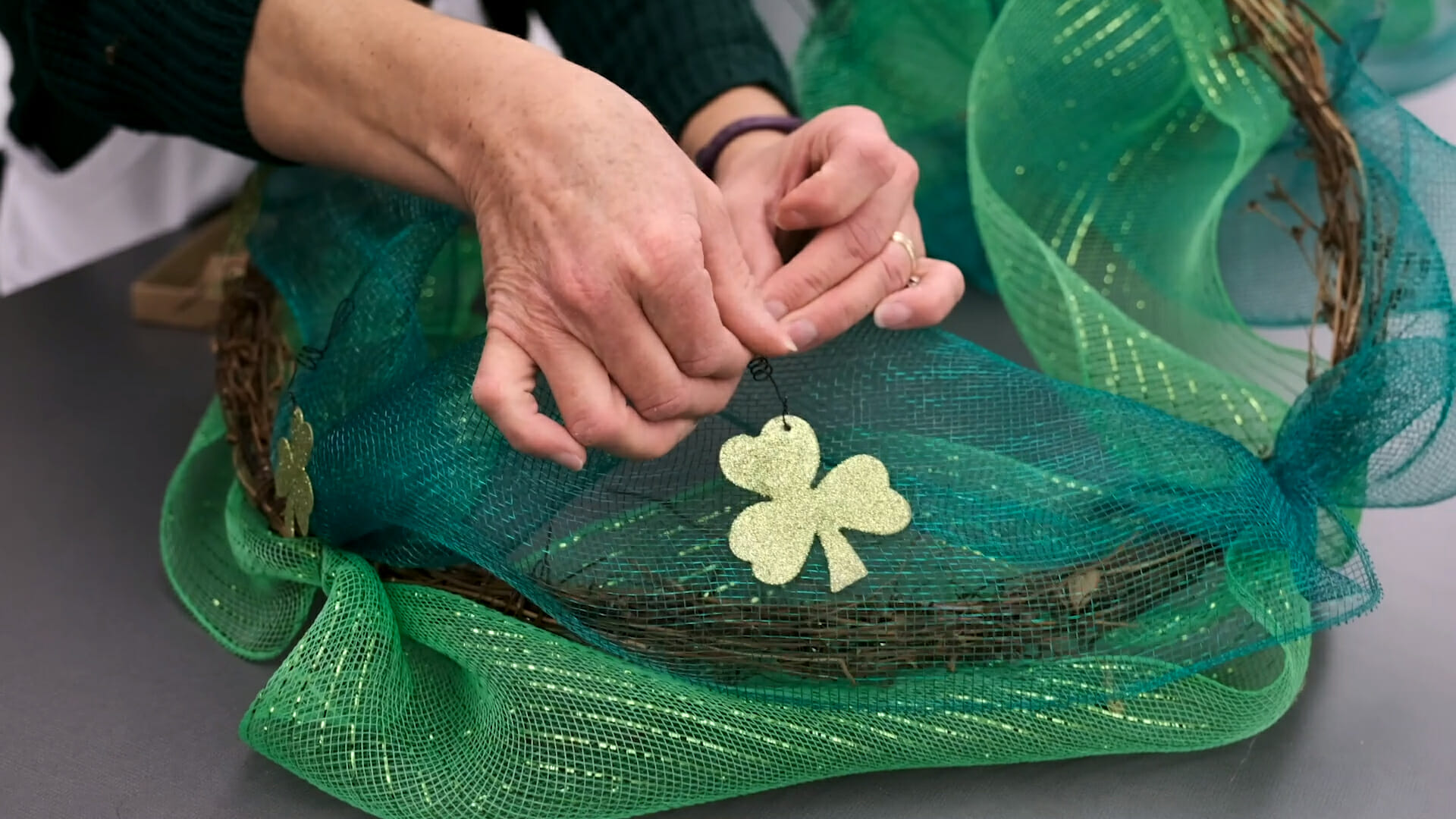 Close-up view of hands attaching glitter shamrocks to a grapevine garland with two shades of green netting.