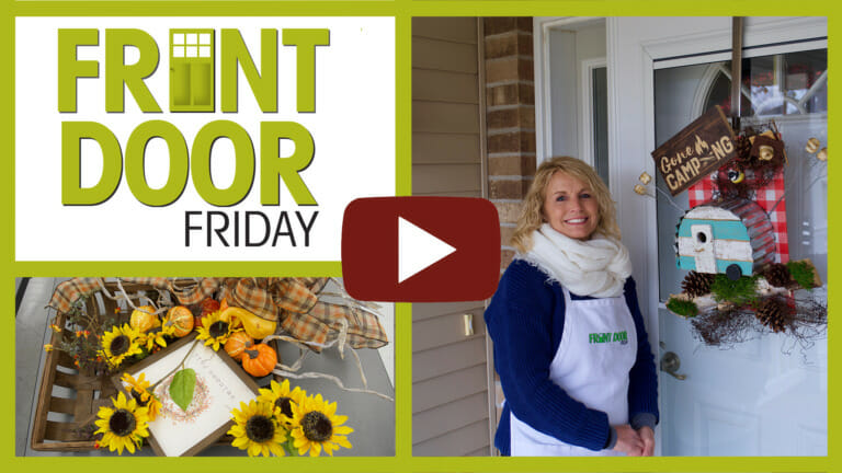 woman on porch with a wreath adorned with red plaid material, pinecones and gone camping sign and camper