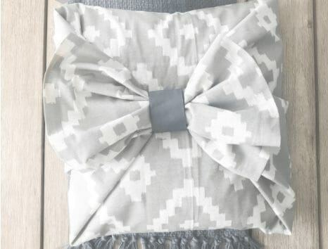 A grey and white print pillow with a large fabric bow.