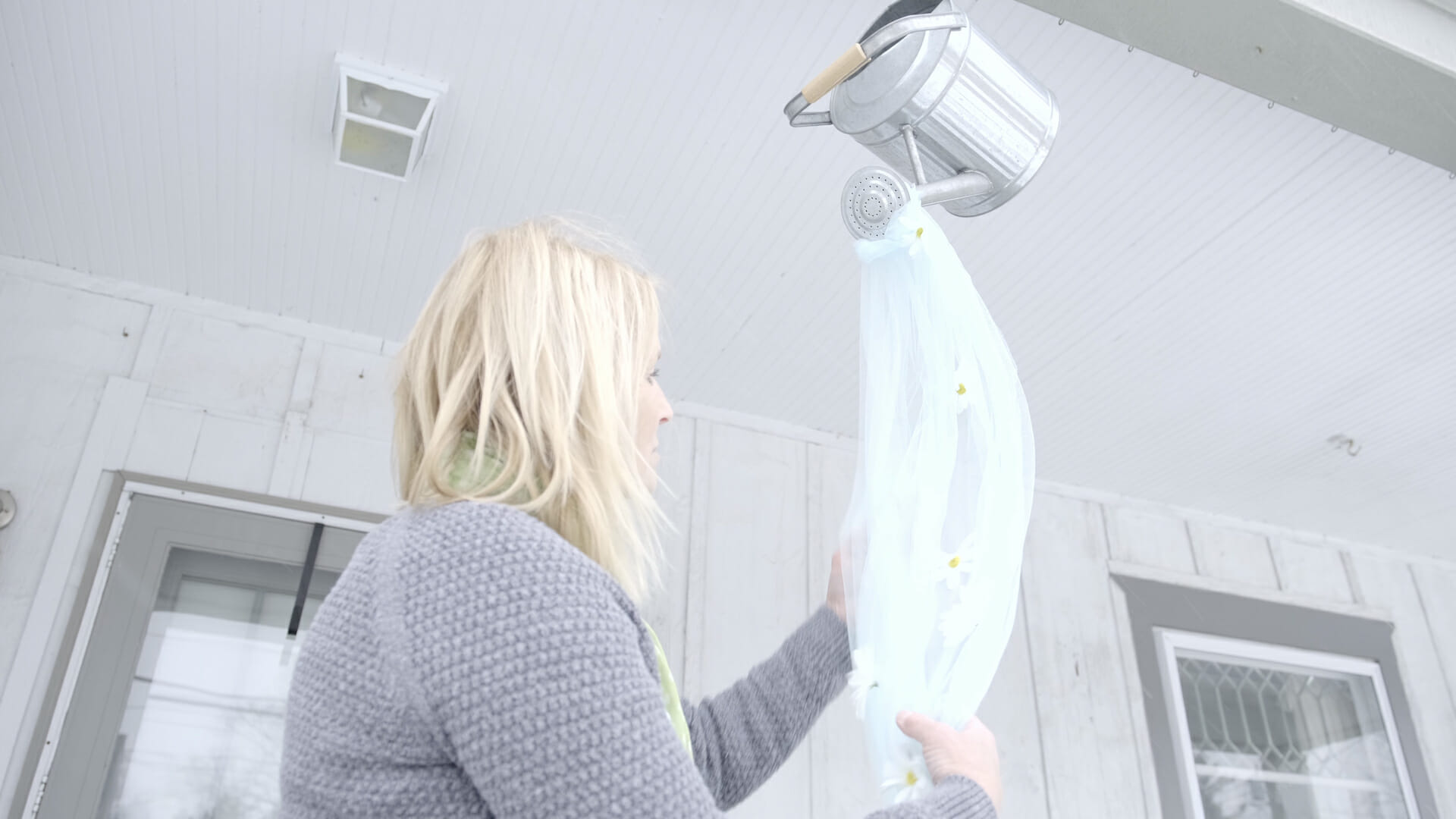 woman hanging a watering can with daisies and tulle fabric