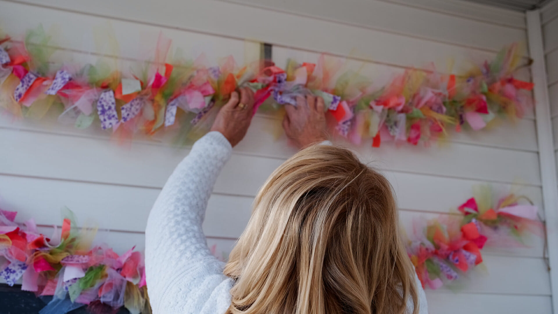 A blonde woman putting up rag garlands made from colorful tulle squares and calico cut with pinking shears.