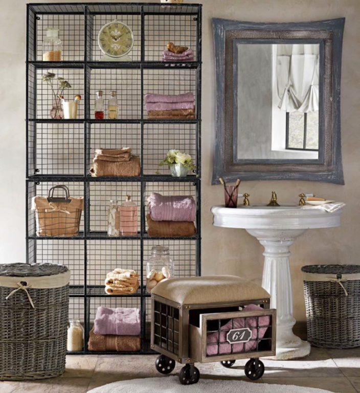Wire cubicle shelving holding bathroom decor and towels, a rustic framed wall mirror, wicker baskets, and pedestal sink.