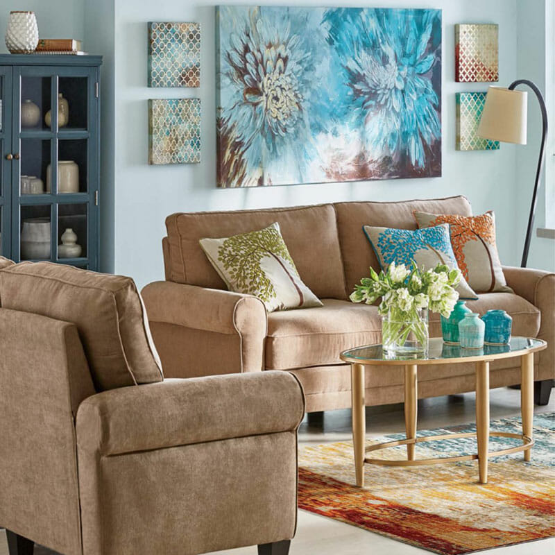 Large wall canvas of two blue mums and four small abstract prints, a tan chair and sofa with three accent pillows.