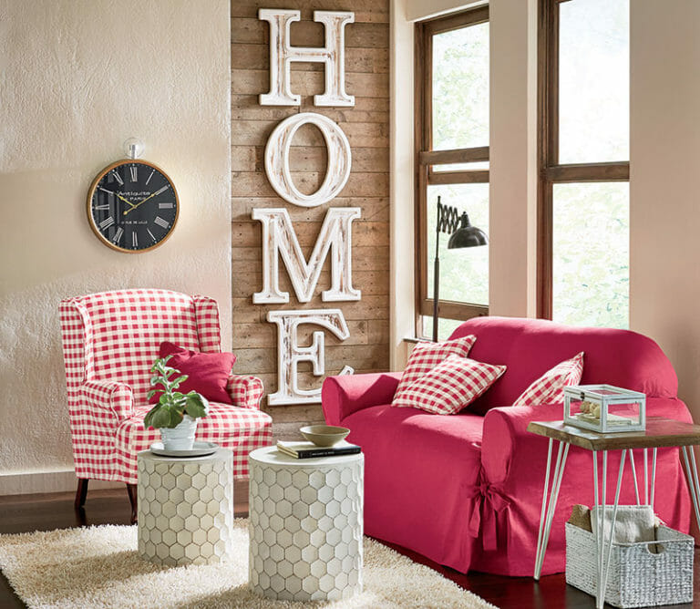 A sofa and chair in solid red and red and white checks, HOME wall art, two white cylinder side tables and a round clock.