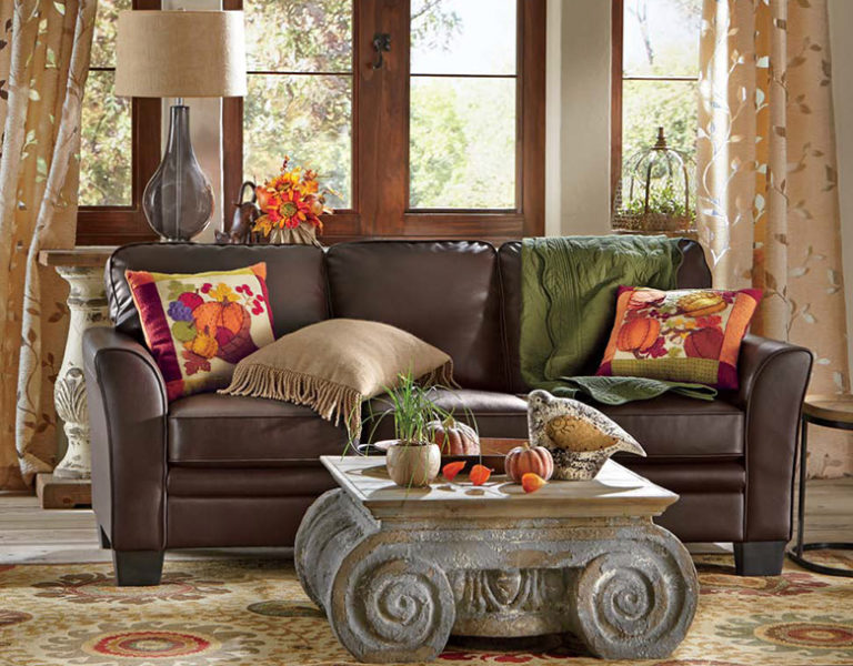 Brown leather sofa with Fall accent pillows, a scroll faux cement coffee table, and beige curtains in a silver vine pattern.