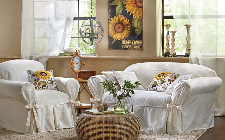 White slipcovered chair and sofa, round rattan coffee table, sunflower wall canvas, sunflower pillows, and a table clock.