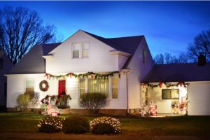 A white two-story house decorated for Christmas at dusk, including garlands, a wreath, lights, and outdoor decor.