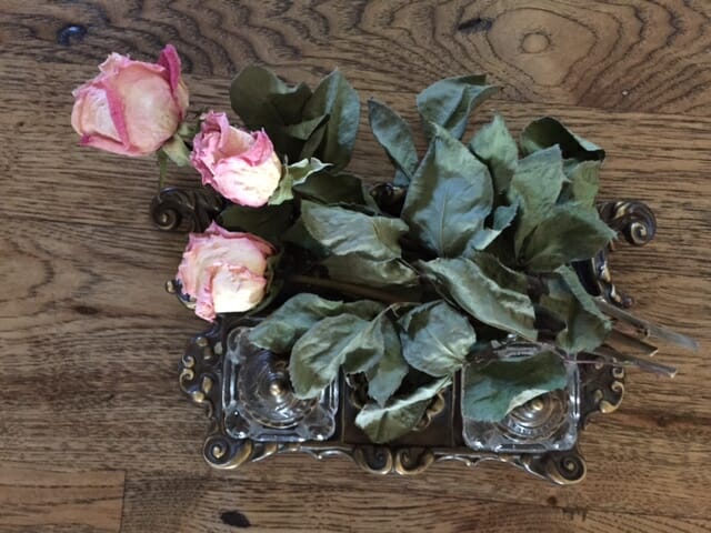Three dried pink roses with leaves and stems, placed on a Victorian tray.