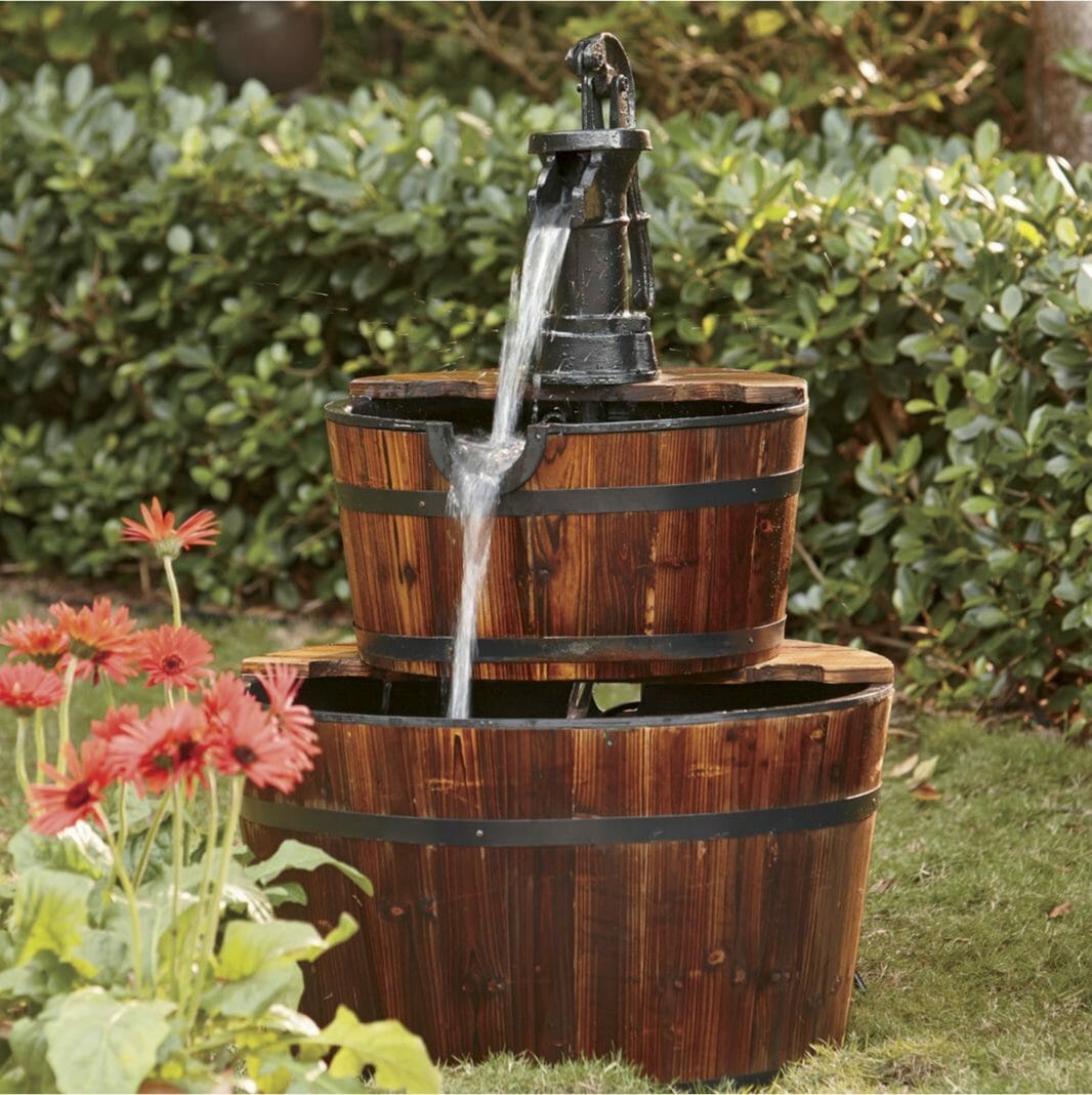 A Farmhouse garden fountain with two tiers of half wooden barrels and a top metal hand pump with flowing water.