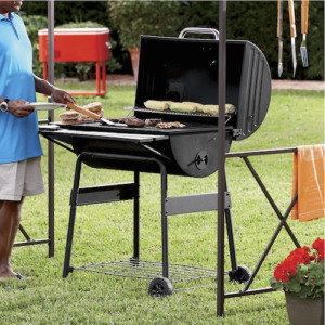 An African-American man turning burgers on a black grill smoker, with corn on the cob on an upper shelf.