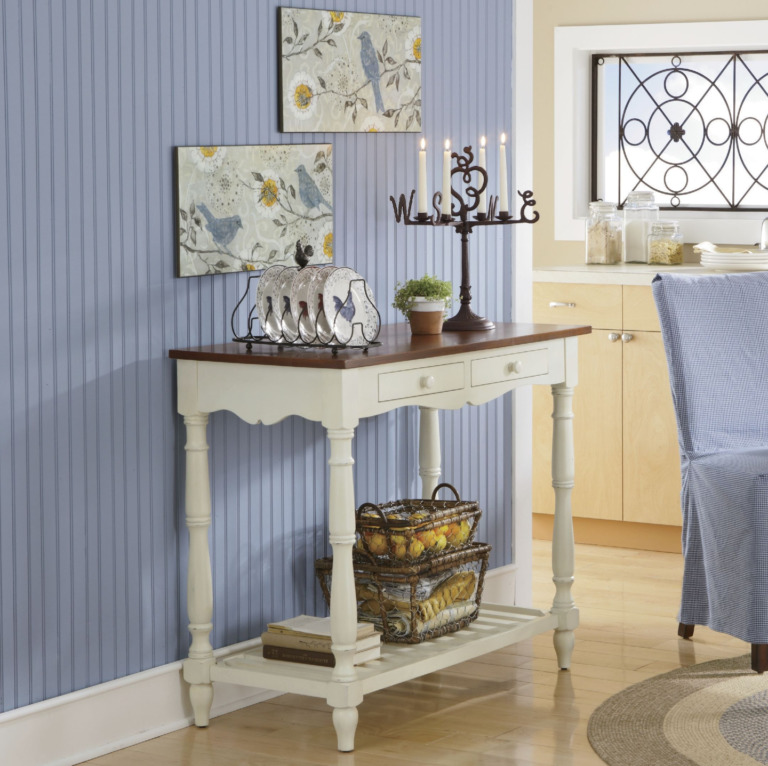 A white console with a candelabra, against a wall with blue wallpaper and blue bird prints, and a blue chair.