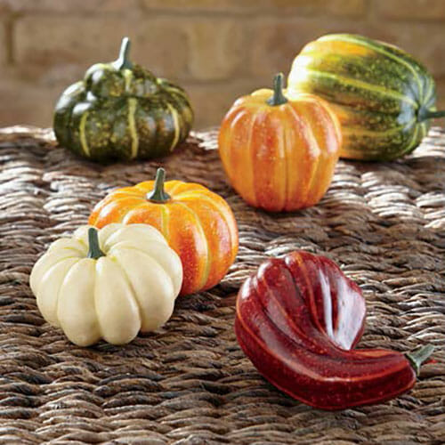 Six colorful pumpkins and gourds on a woven basket top.