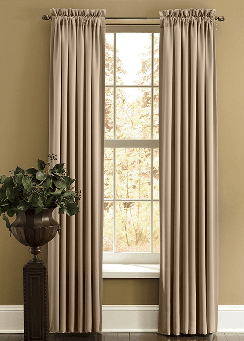 Two tan shirr-on blackout panels on a sunny window, next to a pedestal urn filled with greenery.