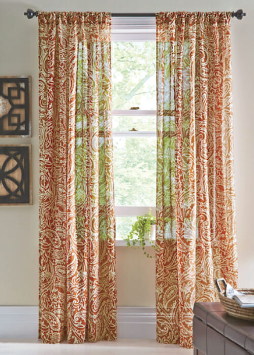 Sheer shirr-on drapes in an orange paisley pattern, by two black and wood geometric wall plaques. 