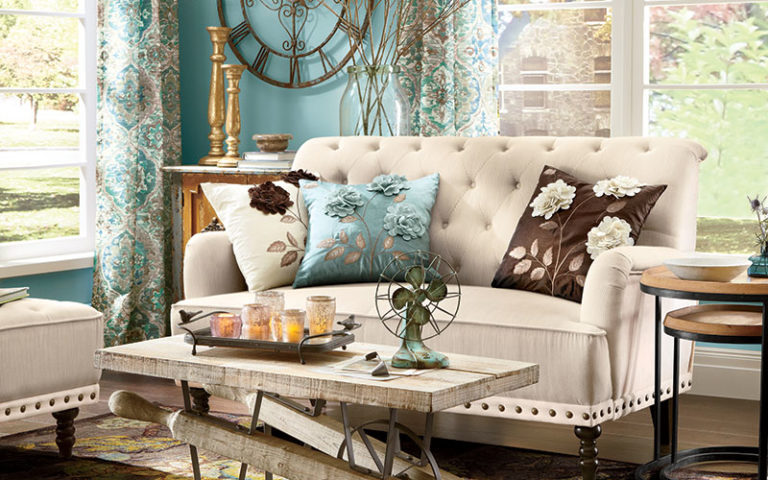 An ivory tufted sofa and chair with floral pillows in ivory, blue and brown, and a rustic wood wheelbarrow coffee table.