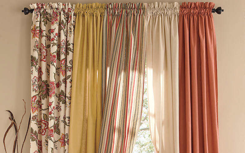 White with red flower pattern, yellow, striped, ivory, and red curtains hanging on window