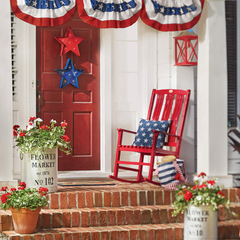 red wooden rocking chair with blue and white stars pillow on a porch with other patriotic décor