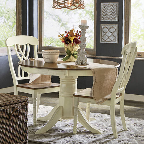 An ivory round wood pedestal dining table and two chairs, with dark stained table top and chair seats, with Fall drieds.
