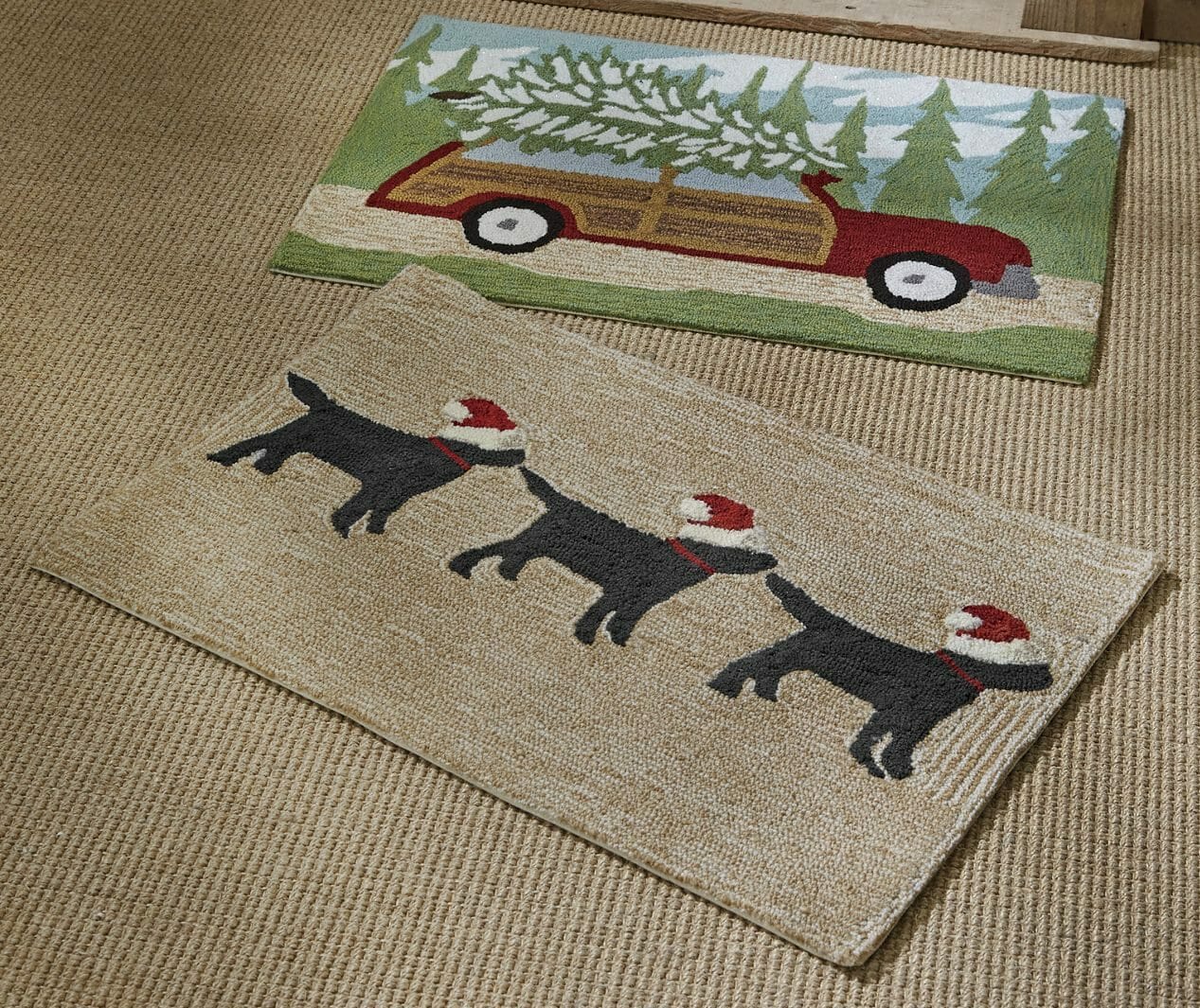 Two indoor/outdoor mats, one with a cut tree on top of a car, one with three black dogs wearing Santa hats.