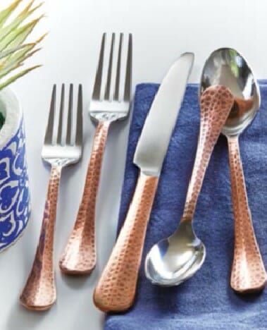 A place setting of copper flatware with hammered copper handles, placed on a royal blue napkin.