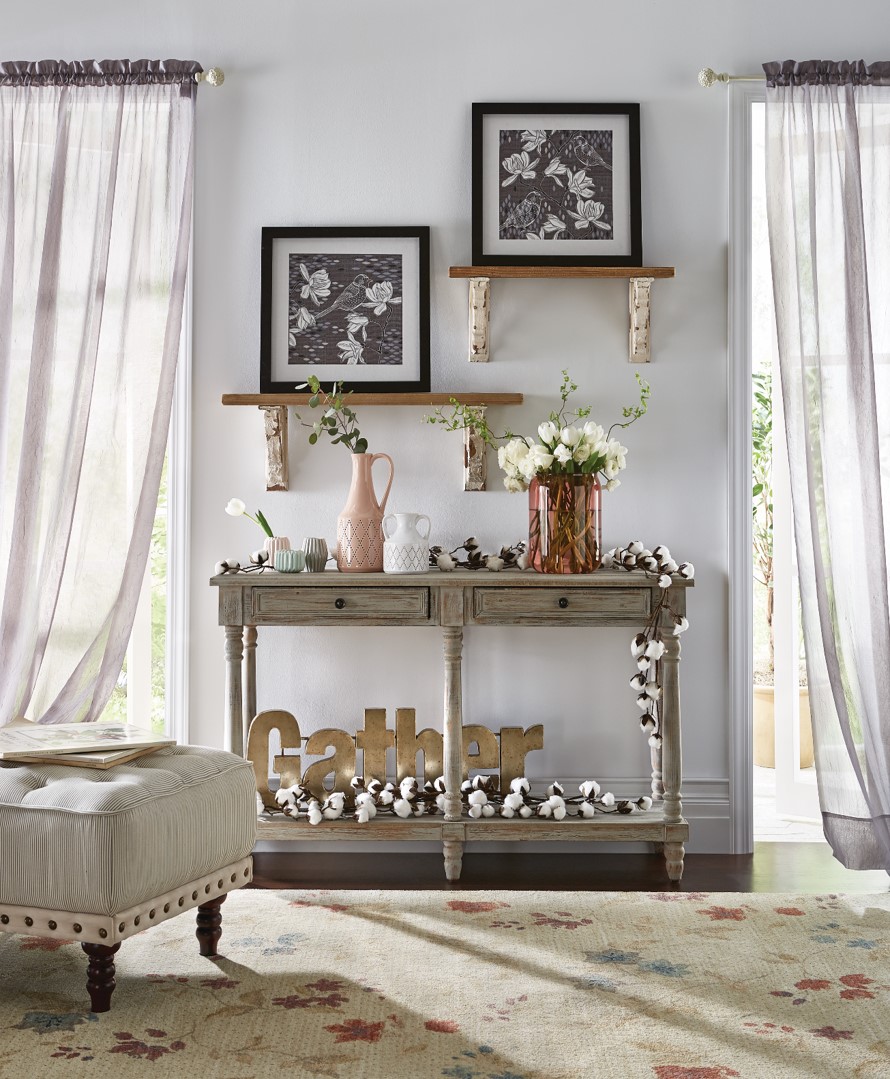 Two framed floral pictures on two shelves above a gray console holding a GATHER sign, vased roses, and cotton branches.