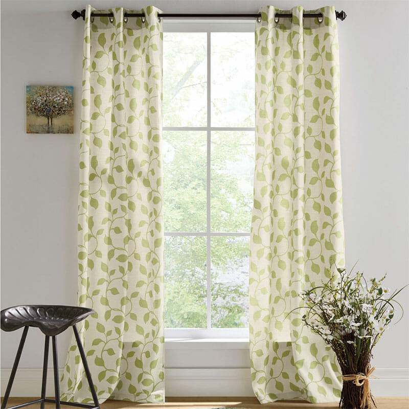 Long grommet curtains in a beige and green vine pattern, a tractor seat stool, a small tree canvas, and bundled twigs.