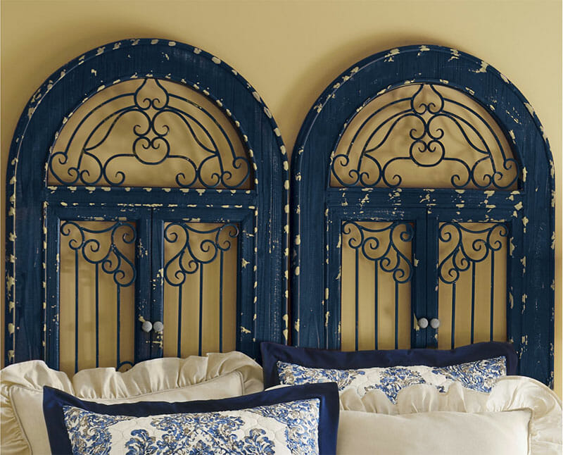 Two distressed navy scroll wall gates, placed on the wall behind a bed as a headboard.