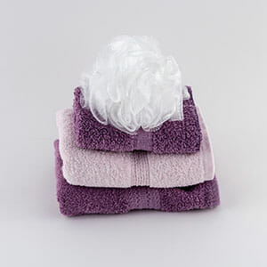 A stack of plum and pink towels, with a white bath pouf on top.