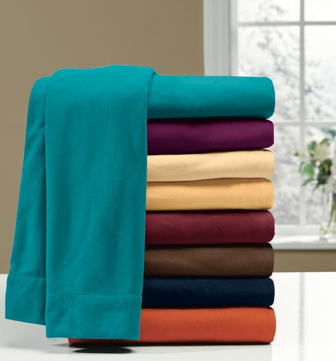 Stacked folded bed sheets on a white counter, in eight bright colors.