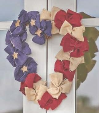 A heart shaped wreath with tied muslin bows in red, tan, and navy blue with tan stars.