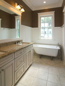 A Farmhouse bathroom with high white wainscot walls, a claw foot tub, and a double sink vanity and mirror.