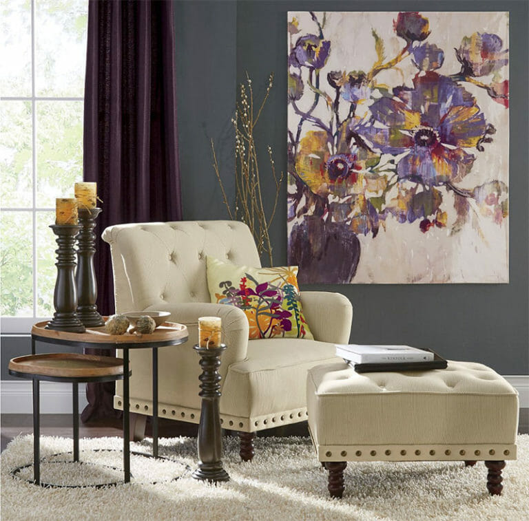 An ivory tufted chair and matching ottoman on a white shag rug, with two nesting side tables, and a large floral canvas.