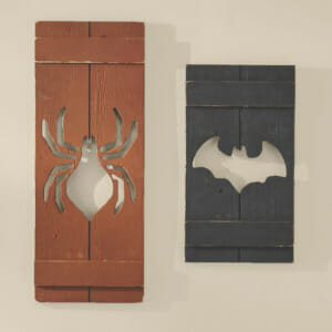 Two wood plank Halloween shutters, a barn red with a spider cutout, and a black with a bat cutout.